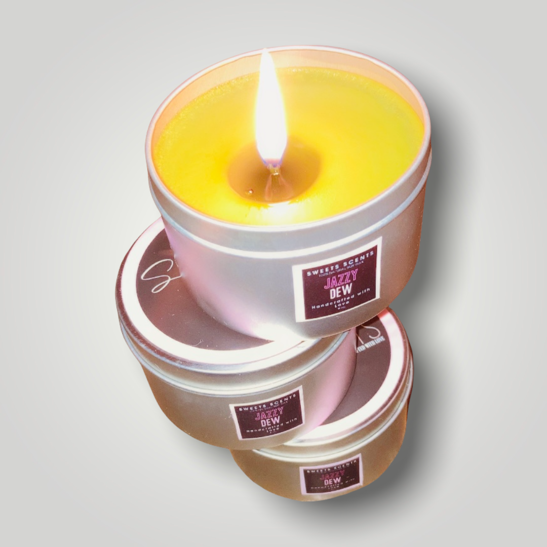 A lit Sweet Scents Jazzy Dew soy candle in a silver travel tin